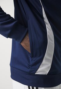 Marinblå sweatshirt med vit sidopanel, strukturerad tyg, långa ärmar och en diskret framficka nära midjan.