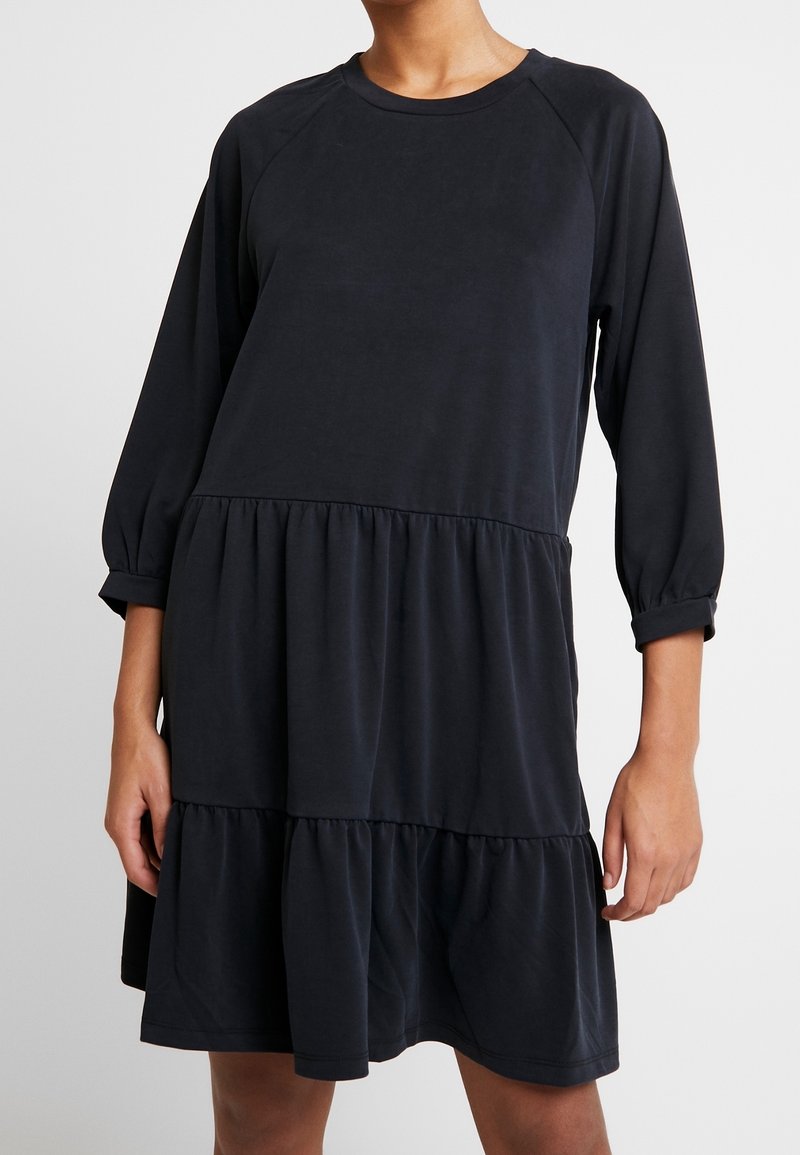 Robe noire à manches trois-quarts en tissu doux, avec un ourlet à volants à étages, un col rond et une coupe décontractée.