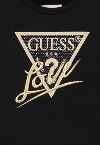 Black sweatshirt featuring a triangular gold and black logo patch with "GUESS" and "LOVE" embroidered in gold cursive.