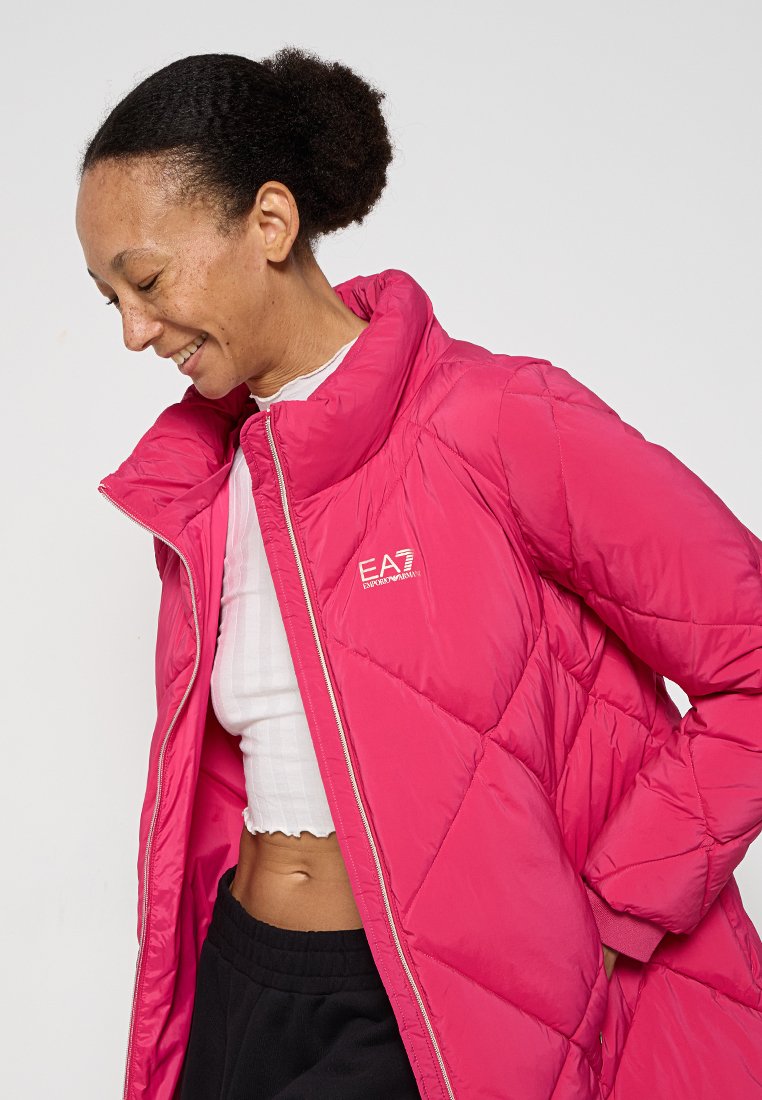 Rosa Pufferjacke mit hohem Kragen, gesteppter Struktur und Reißverschluss vorne. Verfügt über ein Logo auf der Brust und eine glatte, glänzende Oberfläche.