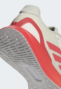 Jasnoszare buty sportowe z czerwonymi akcentami, teksturowana cholewka i podeszwa z gumy o wzorze. Posiadają amortyzowaną piętę i charakterystyczny design boku.