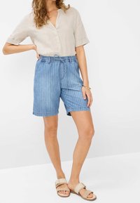 Beige kortärmad skjorta med v-ringning och uppvikta ärmar, tillsammans med blå randiga denimshorts med resårmidja och snörning.