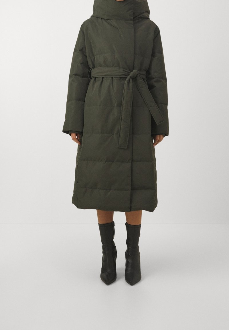 Dlouhý zeleno-olivový péřový kabát s páskem, kapucí a širokými rukávy. Texturovaná látka má vodorovné prošívání a měkký povrch.
