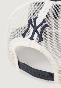 Beisbola cepure ar baltu tīkla aizmuguri un melnu regulējamu siksniņu. Aizmugurē ir izšūts tumši zilas krāsas "NY" logotips.