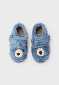Zapatillas de felpa azules con diseño de cara de oso, con textura esponjosa, forma redonda y suelas moradas. Tejido suave con un patrón facial amigable.