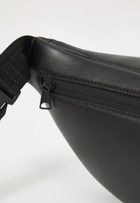 Schwarzer, strukturiert aussehender Kunstleder-Hüftgurt mit einem Reißverschlussfach und verstellbarem Gurt, der eine glatte, geschwungene Form und einen rechteckigen Reißverschlussgriff aufweist.