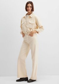 Hellbeige Cordjacke aus Cord mit Knopfverschluss und Brusttaschen, kombiniert mit passenden weitgeschnittenen Hosen, alle mit strukturierter Oberfläche.