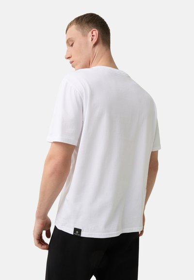 Hvid bomulds t-shirt med korte ærmer, rund hals og et lille sort mærke nederst til venstre. Glat tekstur og afslappet pasform.