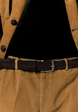 Brune fløjlsbukser parret med et mørkt vævet bælte med en skinnende sølvspænde. Outfitet er lagdelt med en beige jakke og en sort bluse.