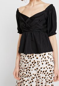 Černá blůza s odhalenými rameny, s nafouknutými rukávy, přiléhavým korzetem a peplum lemem. Hladká tkanina s jemným leskem, překrytá potištěnou sukní.