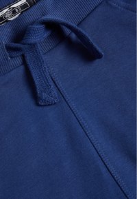 Marineblaue Sweatpants aus einem weichen, leichten Material mit einem gerippten Bund und verstellbarem Kordelzug. Verfügt über eine glatte Textur und minimale Nähte.