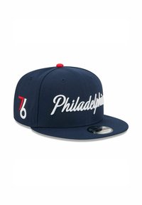 Casquette bleu marine en tissu avec une visière plate. Présente le texte "Philadelphia" brodé en blanc et un bouton accent rouge. Logo "76" audacieux sur le côté.