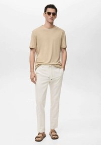Beige short-sleeved t-shirt, cream pinstriped pants, and brown sandals. Accessories include round sunglasses. Casual, relaxed fit.