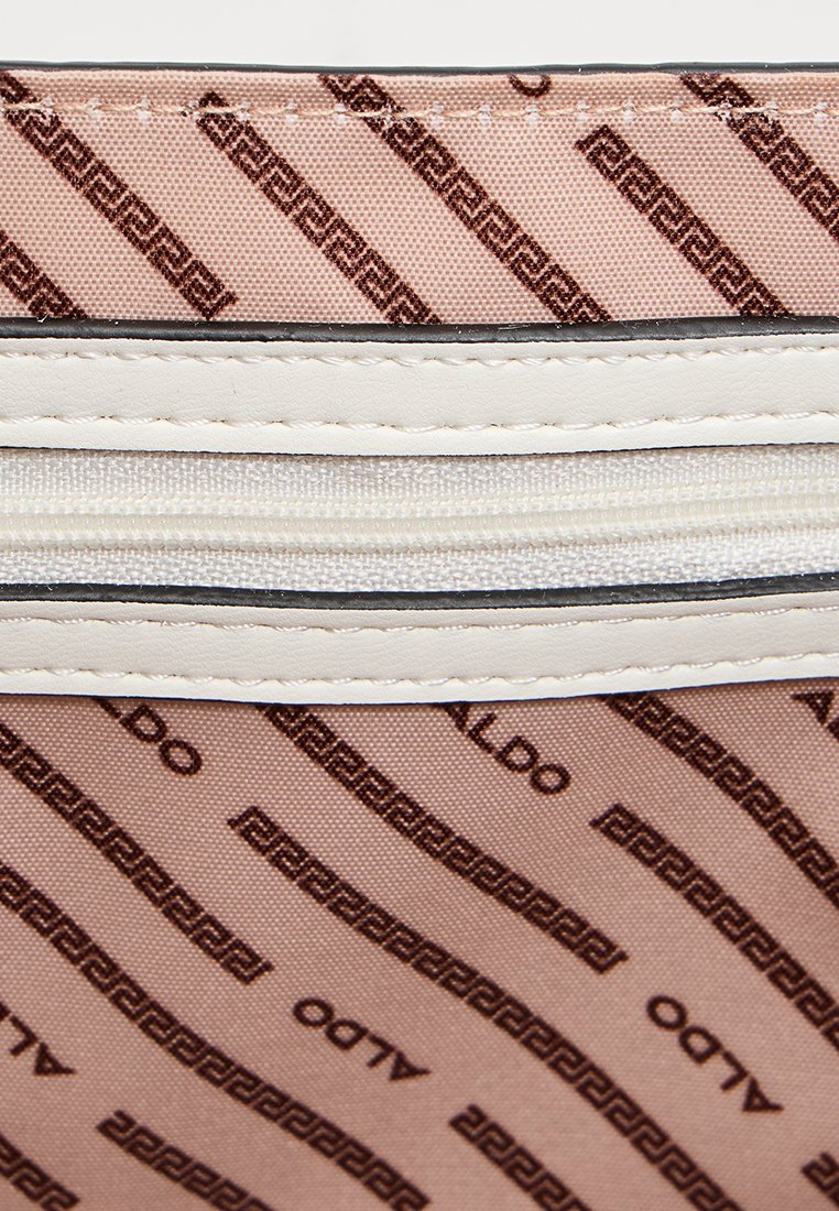 Textile brun à motifs avec des accents de fermeture éclair beige. Présente le logo de la marque et un design de clef grecque disposés en diagonale.