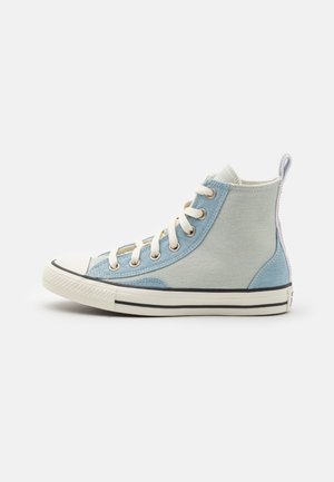 High-top sneakers in light blue canvas with cream accents, white rubber toe, black stripes on sole, and a looped tab at the back.