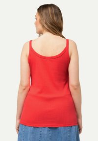 Top rosso a coste con spalline larghe, scollatura rotonda e silhouette aderente, visto da dietro, abbinato a una gonna di denim.