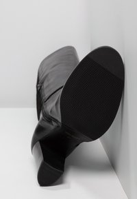 Botín negro de cuero hasta el tobillo con parte superior texturizada, cierre de cremallera y tacón contorneado. La suela tiene un ligero relieve para mayor tracción.