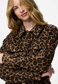 Chaqueta de estampado de leopardo hecha de tela texturizada, con un cuello, cierres de botón y dos bolsillos en el pecho con botones redondos marrones.