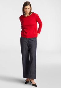 Maglia rossa a maniche lunghe in maglia abbinata a pantaloni larghi in denim scuro e scarpe con tacco nere. Tessuto morbido con una vestibilità comoda.