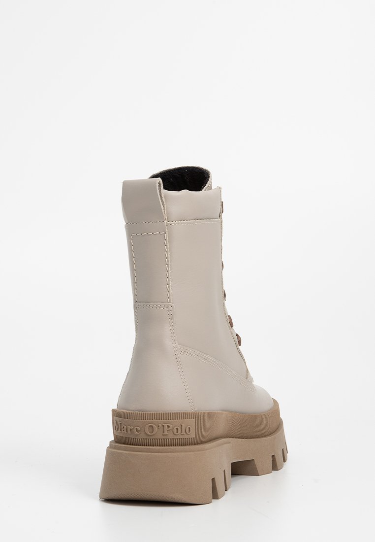 Beige Leder-Ankle-Boots mit einer dicken braunen Gummisohle, Schnürung vorne und verstärktem Absatz. Markenlogo auf der Rückseite der Sohle.