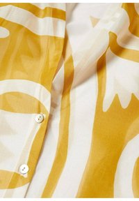 Gelb- und weiß gemusterter Stoff mit einer glatten Textur, der über eine Knopfdetail und ein lässiges, fließendes Design verfügt.