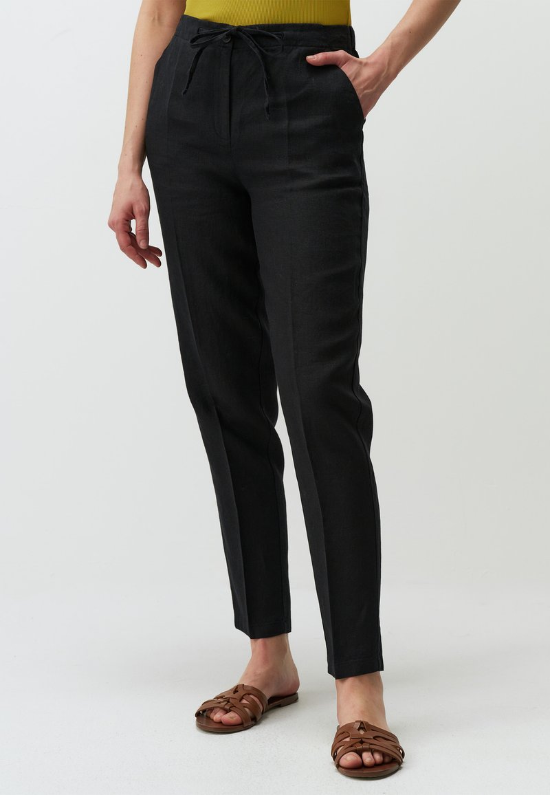 Zwarte linnenbroek met een trekkoord in de taille, slim fit en zijzakken. G gedragen met bruine sandalen met bandjes en een aansluitend gele top.
