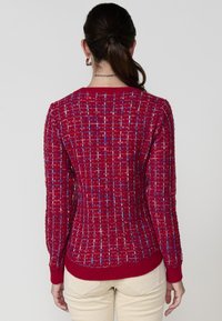 Pull en maille rouge texturée avec un motif à grille comportant des fils bleus et blancs ; manches longues, poignets côtelés et encolure ronde.