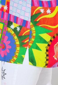 Tissu coloré et à motifs présentant des formes audacieuses telles que des fleurs et un soleil, avec des accents de vert, rouge, rose et jaune sur une base blanche.