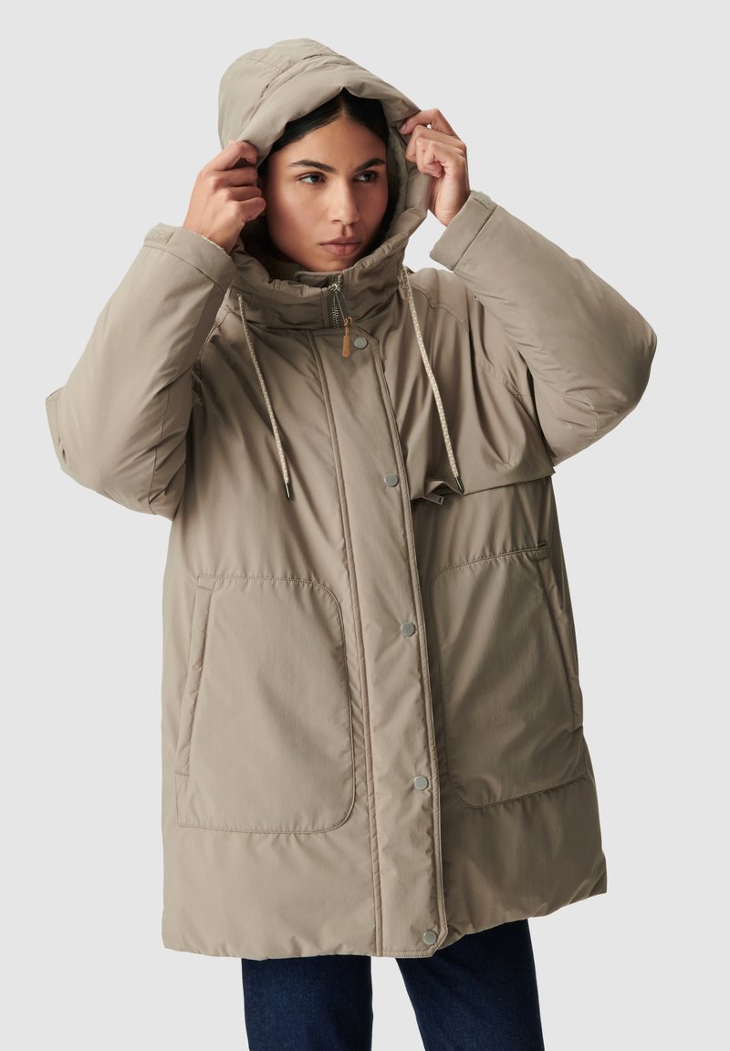 Cappotto piumino oversize beige con cappuccio regolabile, due grandi tasche frontali e chiusura a bottoni a pressione. Superficie liscia e opaca.