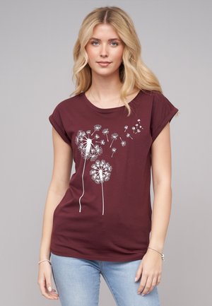 T-shirt bordeaux avec des manches courtes retroussées, présentant un graphisme de pissenlit blanc et de graines en vol. Fabriqué en tissu en coton doux.