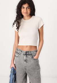 Short-sleeve, ribbed beige cropped t-shirt with "element" logo. Paired with high-waisted faded gray jeans and a blue shoulder bag.