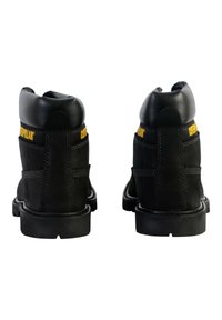 Black suede and leather work boots with yellow "Caterpillar" branding, featuring padded collar, stitching details, and durable soles.