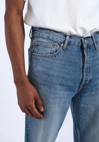 Jeans in denim blu chiaro con una vestibilità rilassata, cinque tasche e dettagli in metallo color rame. Il tessuto presenta una classica texture consumata.