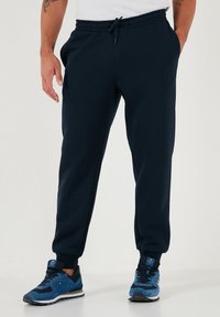 Navyblauwe trainingsbroek met elastische taille, verstelbare trekkoord, zijzakken en geribbelde boorden. G gedragen met blauwe sportschoenen.