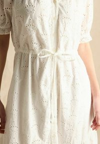 Weißes Blusenkleid mit gestickten Blumenmustern, kurzen Ärmeln, einer Knopfleiste und einem verstellbaren Kordelzug in der Taille.