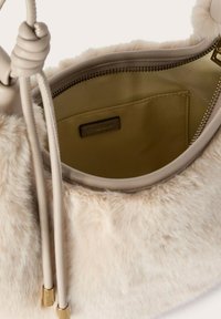 Hellbeige Kunstpelz-Handtasche mit glattem Innenfutter, Reißverschluss und knotigem Griffdetail. Das Innere verfügt über eine kleine Tasche.