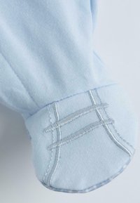 Poignet de chemise bleu clair présentant une texture lisse, décoré de coutures argentées dans un motif unique le long du bord.