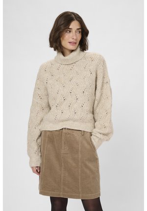 Beige stickad tröja med hög krage och texturmönster, tillsammans med en brun manchesterkjol. Mjuk tyg och lös passform.