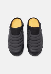 Fekete slip-on cipők steppelt felsőrésszel és texturált gumitalppal. Párnázott nyakkal és sárga béléssel rendelkezik. Minimalista dizájn.