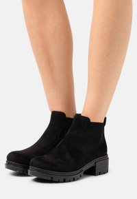 Bottines en suede noir avec des panneaux latéraux élastiques, une semelle texturée et un talon épais. Fini lisse avec des détails de surpiqûre contrastants.