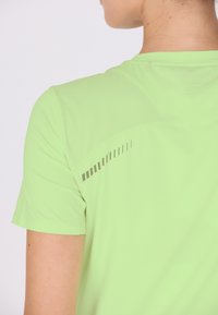 Kortærmet atletisk skjorte i lysegrøn med en struktureret overflade og reflekterende grå detaljer på den øvre ryg for synlighed.