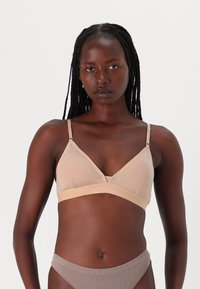Bralette beige avec un design triangulaire, des bretelles réglables et un tissu sans couture. Il présente une bande sous la poitrine douce, une texture lisse et des coutures minimalistes.