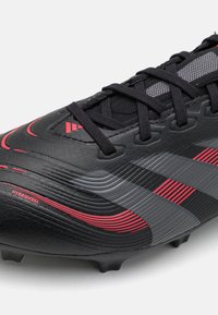 Svarta fotbollsskor med texturerad ovandel, röda och grå detaljer samt snörningsdesign. Funktioner små formade dobbar på sulan för bättre grepp.