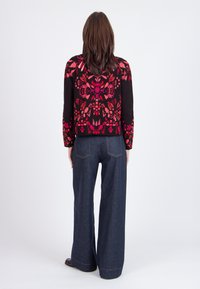 Suéter negro con un patrón floral rojo, manga larga y pantalones de denim oscuros de corte recto. El conjunto presenta un ajuste relajado y detalles mínimos.