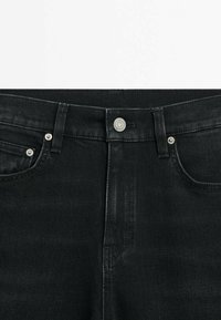 Jean en denim noir avec braguette à boutons, design à cinq poches et couture ton sur ton. Le tissu a une texture lisse avec un léger stretch.