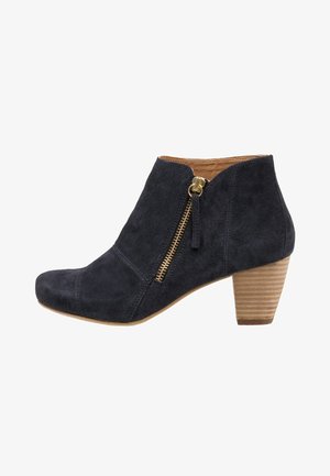 Naiskengän mustat mokkanahkaiset nilkkurit, joissa on pinoitu puinen korko ja kullanvärinen sivuvetoketju, jossa on vetotappi.