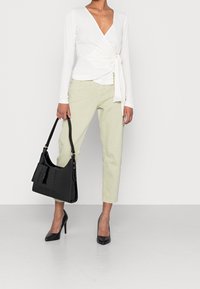 Top avvolgente bianco a maniche lunghe, jeans a sigaretta verde chiaro, borsa a spalla nera con texture coccodrillo e scarpe con tacco nere.