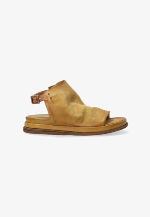 Tan lædersandal med åben tå, slouchy overdel og justerbar spænde. Flad sål med let tekstur langs kanten.