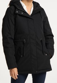 Veste d'hiver noire avec capuche, dotée d'une fermeture éclair, de cordons de serrage réglables, de deux poches latérales et d'une surface extérieure texturée.