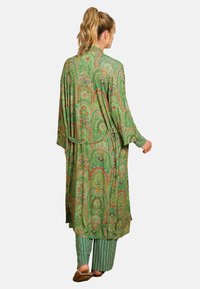 Long green robe featuring an intricate paisley pattern in orange and cream, with a tie belt and wide sleeves, paired with striped green pants.